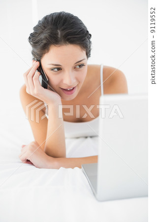 Cheerful casual brunette in white pajamas making a phone call an Cheerful casual brunette in white pajamas making a phone call an 9119552