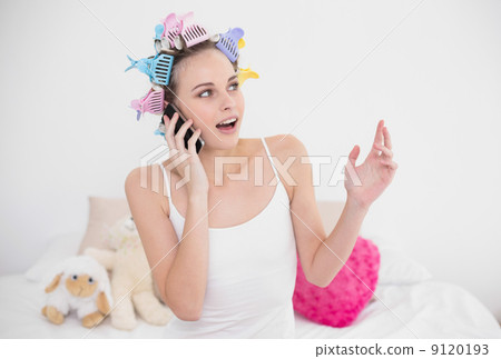 Surprised natural brown haired woman in hair curlers making a ph 9120193