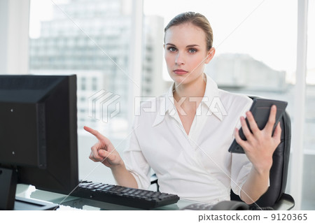 Frowning businesswoman holding calculator sitting at desk lookin 9120365