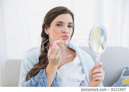 Pouting casual brown haired woman in white pajamas applying glos 9121997