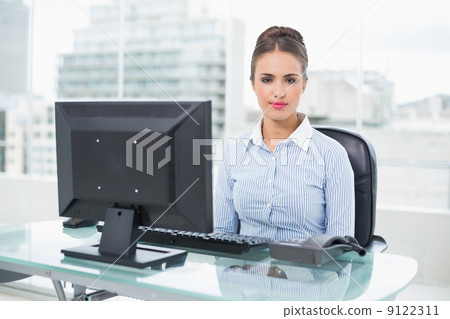 Calm brunette businesswoman sitting at her desk Calm brunette businesswoman sitting at her desk 9122311