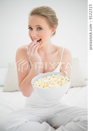 Natural happy blonde eating popcorn on bed 9122315