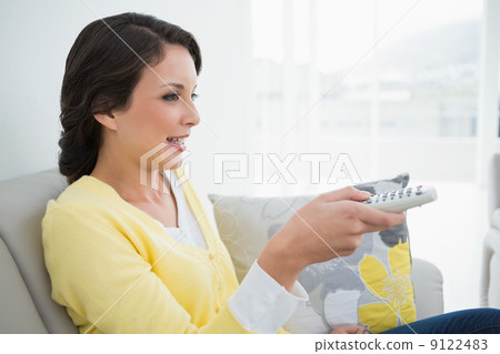 Peaceful casual brunette in yellow cardigan changing tv channel Peaceful casual brunette in yellow cardigan changing tv channel 9122483