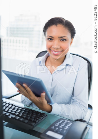 Smiling young dark haired businesswoman using a tablet pc Smiling young dark haired businesswoman using a tablet pc 9122485