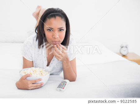 Peaceful young dark haired model eating popcorn while watching t 9122585