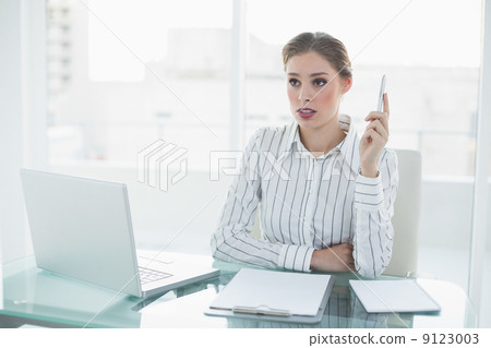 Beautiful thinking businesswoman holding a pen sitting at her de 9123003
