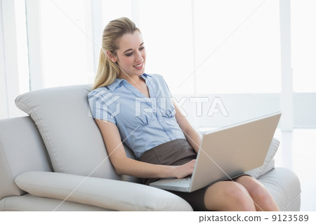 Cheerful classy businesswoman sitting on couch using her noteboo 9123589
