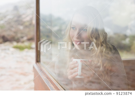 Woman with coffee cup looking out through cabin window 9123874