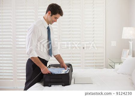 Smiling businessman unpacking luggage at a hotel bedroom 9124230