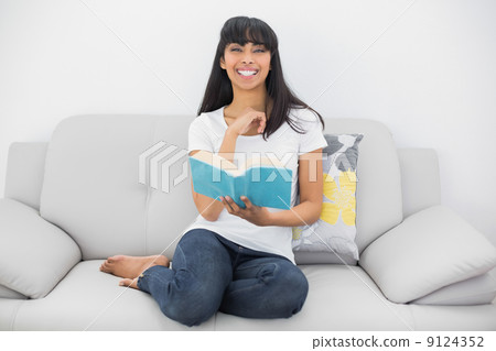 Beautiful smiling woman sitting on couch holding a book 9124352