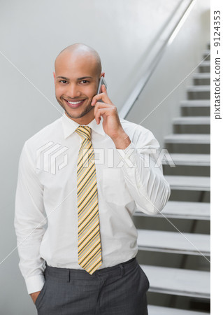 Smiling businessman using cellphone against staircase 9124353
