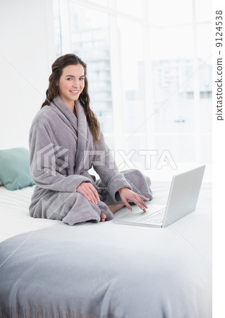 Smiling brunette in bathrobe using laptop in bed 9124538