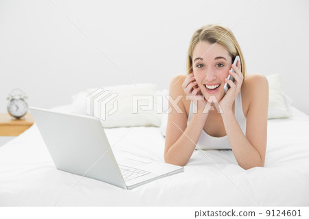 Amused calm woman phoning lying on her bed next to her laptop 9124601