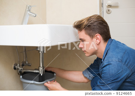 Handsome plumber repairing the drain of sink 9124665