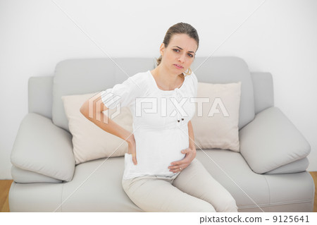 Suffering pregnant woman looking seriously at camera touching he Suffering pregnant woman looking seriously at camera touching he 9125641