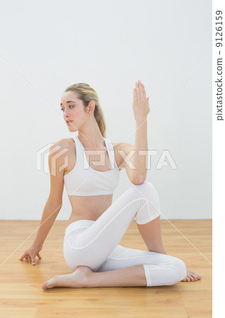 Serious ponytailed woman sitting on floor stretching her body 9126159