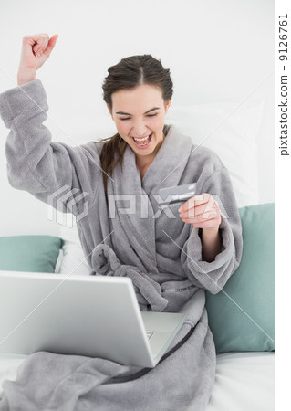 Excited woman in bathrobe doing online shopping in bed 9126761