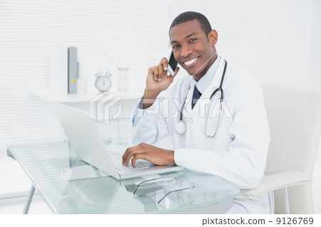 Smiling male doctor using cellphone and laptop 9126769