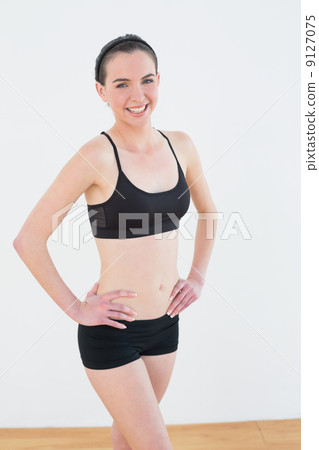 Smiling toned woman with hands on hips in fitness studio 9127075