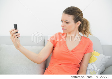 Pretty serious woman looking at her smartphone sitting on couch 9127279