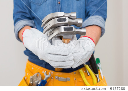 Mid section of handyman holding hammers with toolbelt around wai 9127280