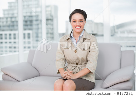 Smiling well dressed woman sitting on sofa at home 9127281