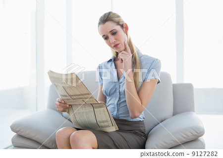 Thoughtful lovely businesswoman reading newspaper while sitting 9127282