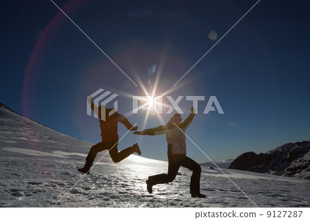Silhouette couple jumping on snow against sun and blue sky 9127287