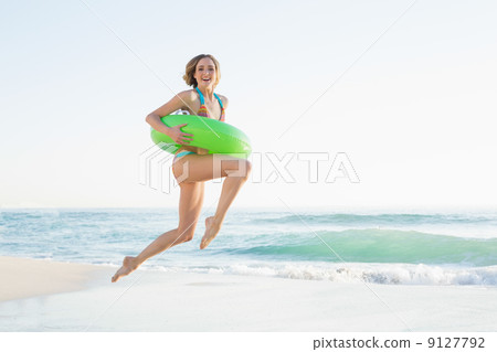 Pretty young woman holding a rubber ring while jumping on beach Pretty young woman holding a rubber ring while jumping on beach 9127792