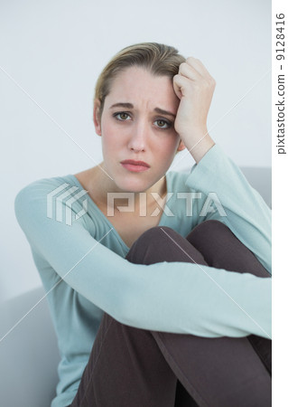 Natural young woman sitting worried on couch Natural young woman sitting worried on couch 9128416
