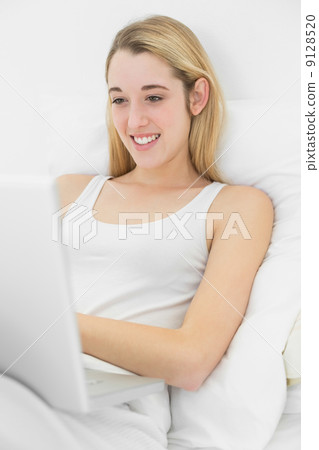Content young woman working with her notebook lying on her bed 9128520