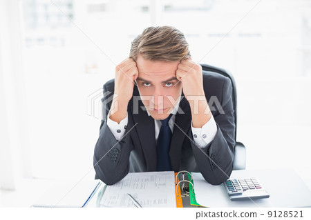 Portrait of worried businessman sitting at office desk 9128521