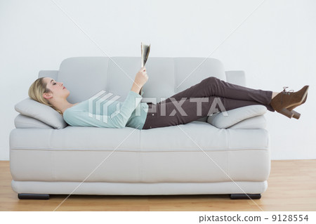 Attractive blonde woman reading newspaper lying on couch Attractive blonde woman reading newspaper lying on couch 9128554