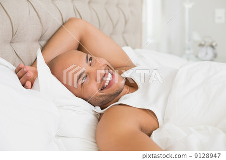 Smiling young bald man resting in bed Smiling young bald man resting in bed 9128947