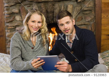 Lovely couple using tablet PC in front of lit fireplace Lovely couple using tablet PC in front of lit fireplace 9128963
