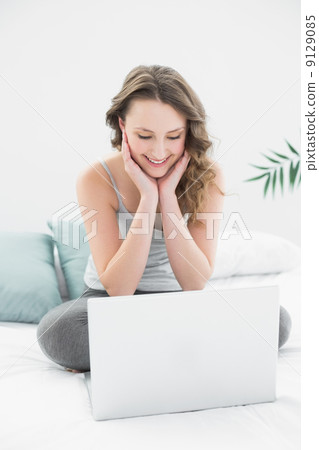 Smiling casual brunette looking at laptop in bed Smiling casual brunette looking at laptop in bed 9129085