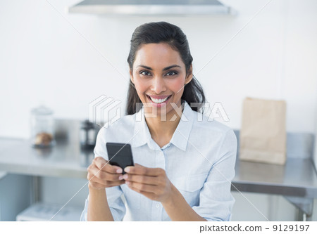Natural smiling woman holding her smartphone looking at camera Natural smiling woman holding her smartphone looking at camera 9129197