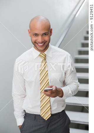 Smiling businessman text messaging against staircase 9129451