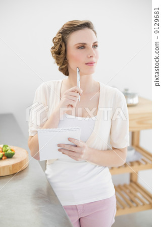 Thinking woman standing in kitchen writing a shopping list Thinking woman standing in kitchen writing a shopping list 9129681