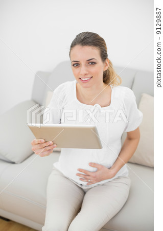 Pregnant woman holding her tablet smiling at camera 9129887