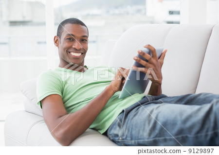 Casual smiling Afro man using digital tablet on sofa Casual smiling Afro man using digital tablet on sofa 9129897