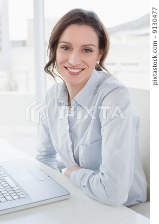 Smiling young businesswoman with laptop in office 9130477