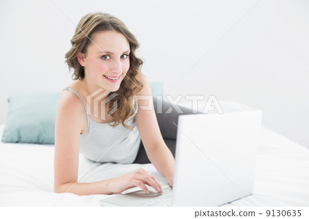 Smiling casual brunette with laptop in bed Smiling casual brunette with laptop in bed 9130635