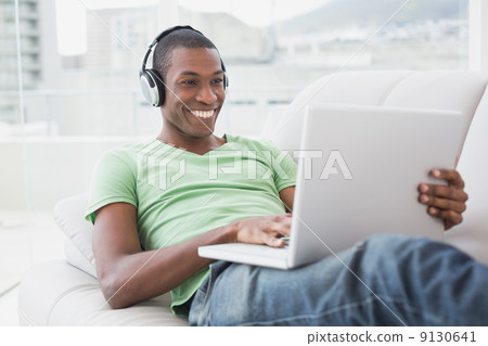 Smiling Afro man with headphones using laptop on sofa Smiling Afro man with headphones using laptop on sofa 9130641