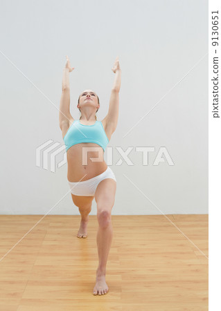 Unsmiling slim blonde standing in high lunge pose 9130651