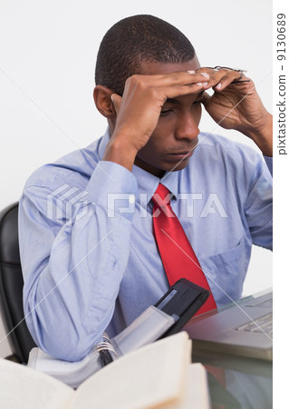 Stock Photo: Frustrated Afro businessman with head in hands at desk