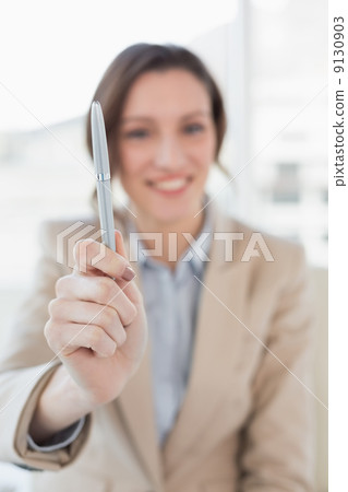 Smiling businesswoman holding out a pen in office 9130903