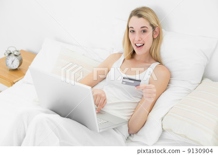 Astonished young woman using her laptop for home shopping while Astonished young woman using her laptop for home shopping while 9130904