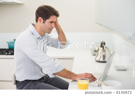 Concentrated casual man using laptop in kitchen 9130972