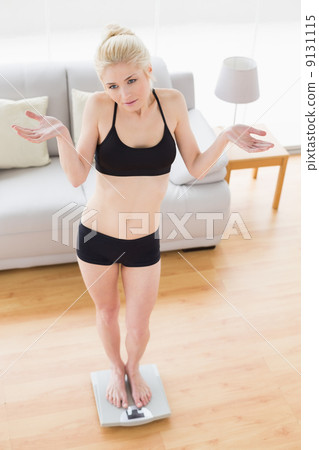Unsure young woman in sportswear standing on scale 9131115